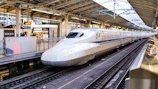 A white Shinkansen bullet train arriving at a modern railway station platform