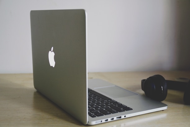 A sleek black Bluetooth headset resting on a wooden desk beside a laptop.