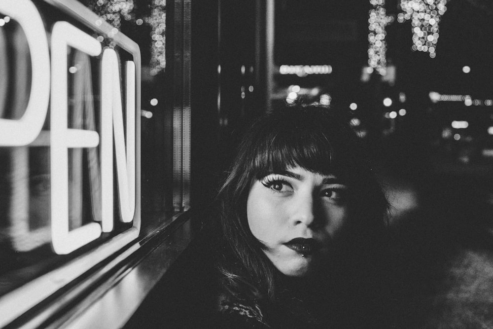 grayscale photo of woman beside open signage