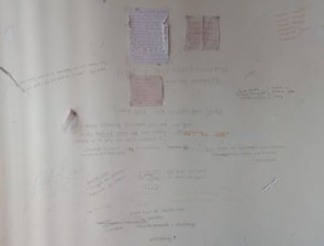 A wall covered in various handwritten motivational quotes and notes. Some quotes are attributed to notable personalities and focus on themes like persistence, success, and self-belief. There are drawings and scribbles, including diagrams and small notes, emphasizing hard work and dedication.