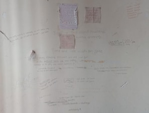 A wall covered in various handwritten motivational quotes and notes. Some quotes are attributed to notable personalities and focus on themes like persistence, success, and self-belief. There are drawings and scribbles, including diagrams and small notes, emphasizing hard work and dedication.
