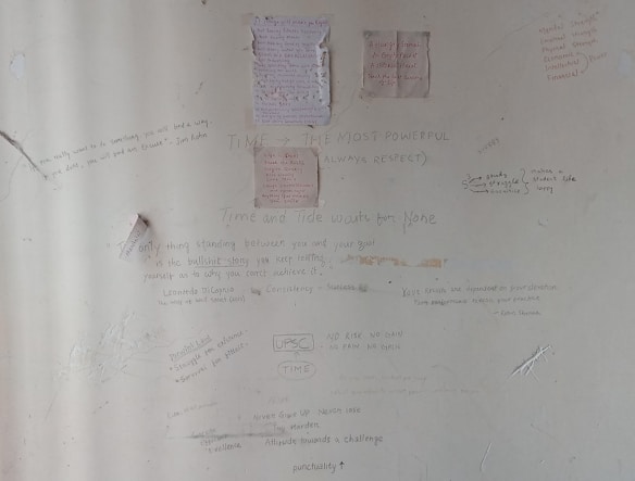 A wall covered in various handwritten motivational quotes and notes. Some quotes are attributed to notable personalities and focus on themes like persistence, success, and self-belief. There are drawings and scribbles, including diagrams and small notes, emphasizing hard work and dedication.