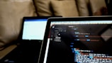 Close-up of hands coding a responsive website on a tablet and laptop.