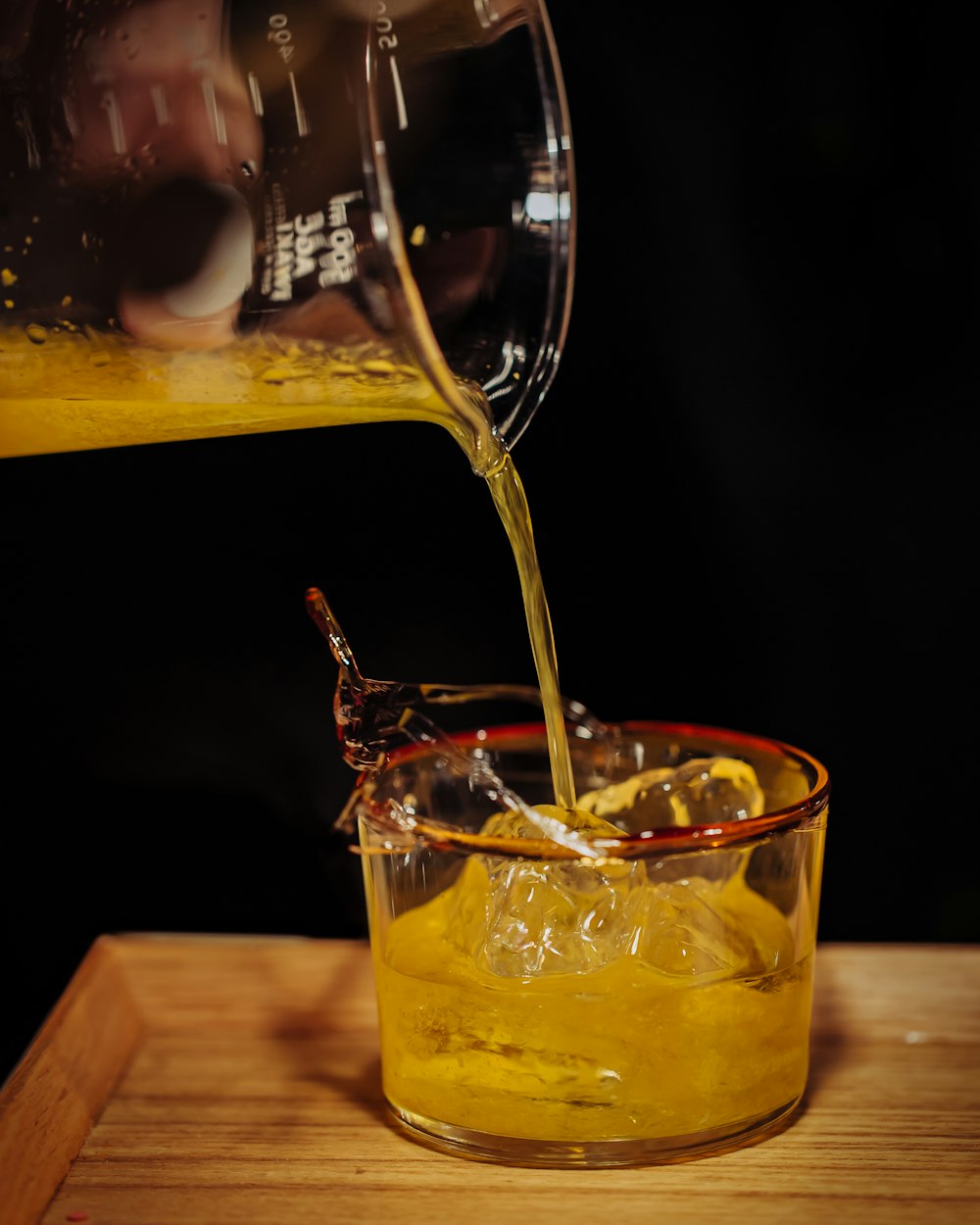 person pouring juice blend on glass filled with ice and juice