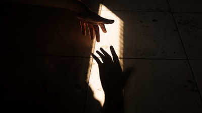 A hand reaching out from shadowy darkness toward a faint glowing object.