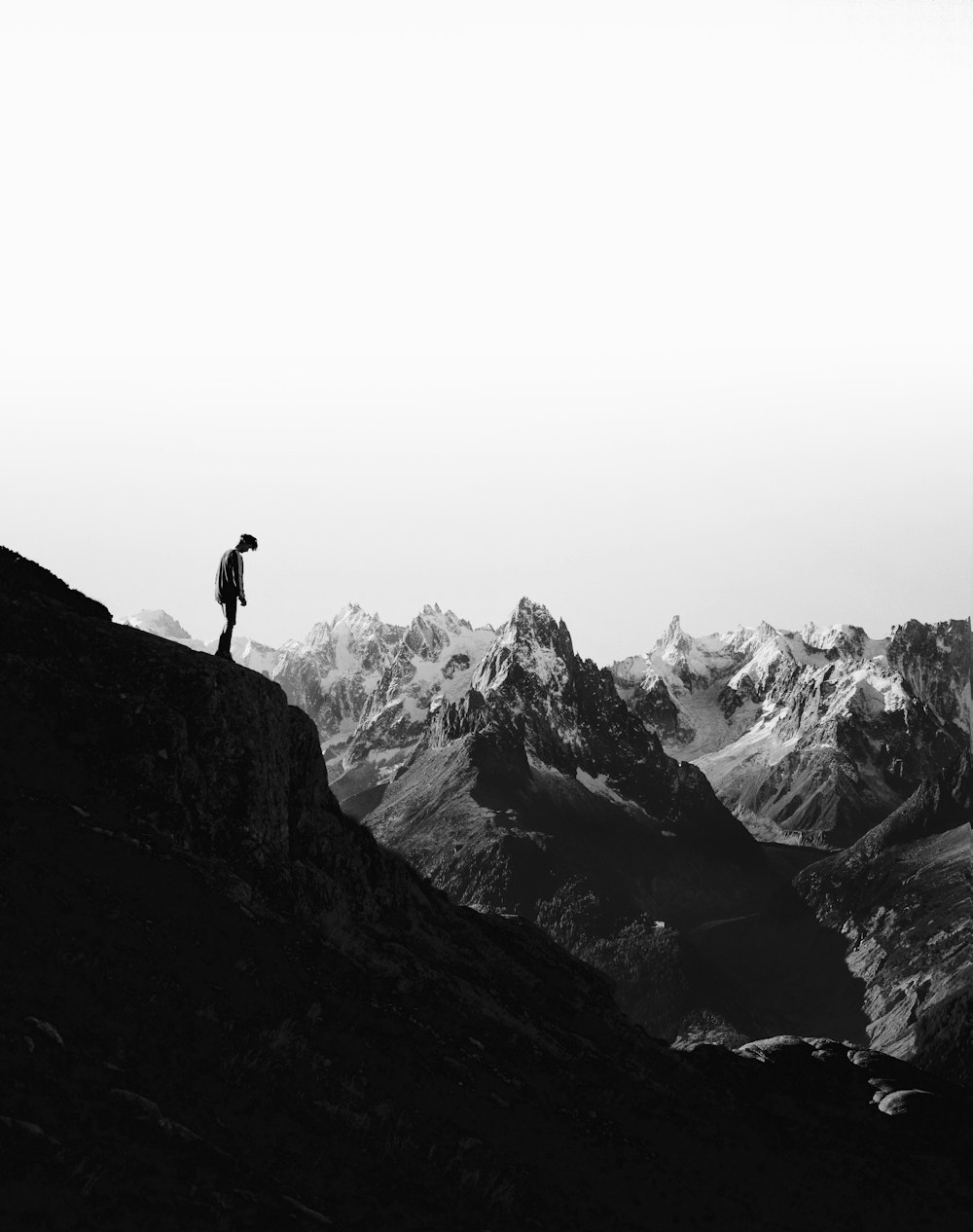 silhouette of person standing on cliff in front of snowed mountains
