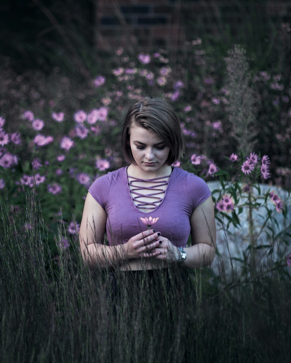 Foto de foco seletivo da mulher em pé no campo de flores verde e rosa durante o dia