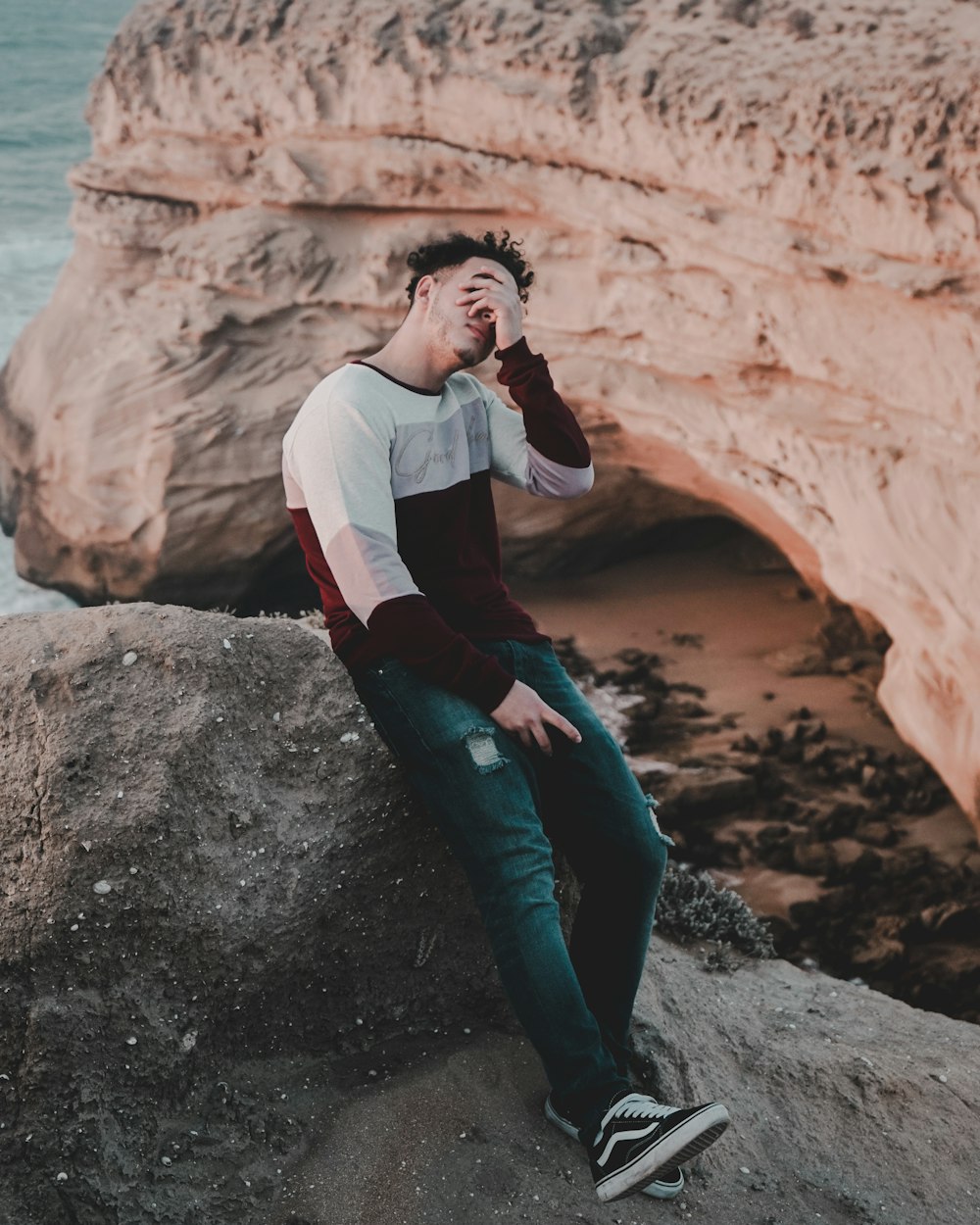 man covering his eyes leaning against rock