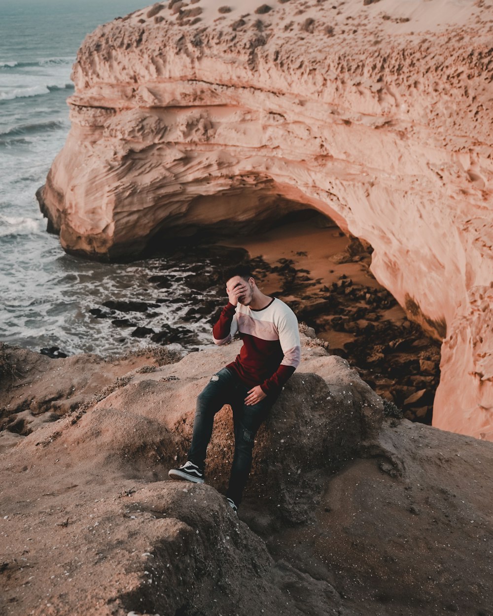 man covering face while sitting near the ocean water