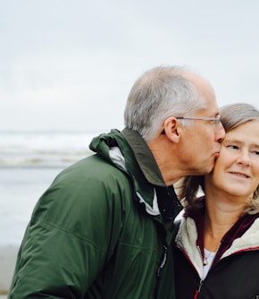 man kissing woman on check beside body of water