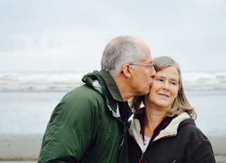 man kissing woman on check beside body of water