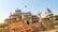 An intricately designed historical building with domes and decorative arches, set against a clear blue sky. Birds are flying around the structure, and a sign in the foreground reads 'Central Museum Jaipur'. The building has detailed architectural elements typical of Indian heritage.
