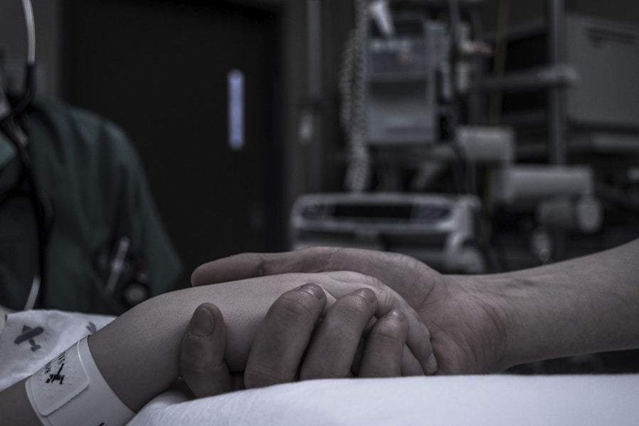 A comforting nurse gently holding an elderly patient's hand in a softly lit home setting.
