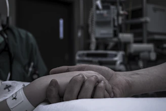A gentle hand resting on another’s in a hospital room, symbolizing comfort and spiritual support.