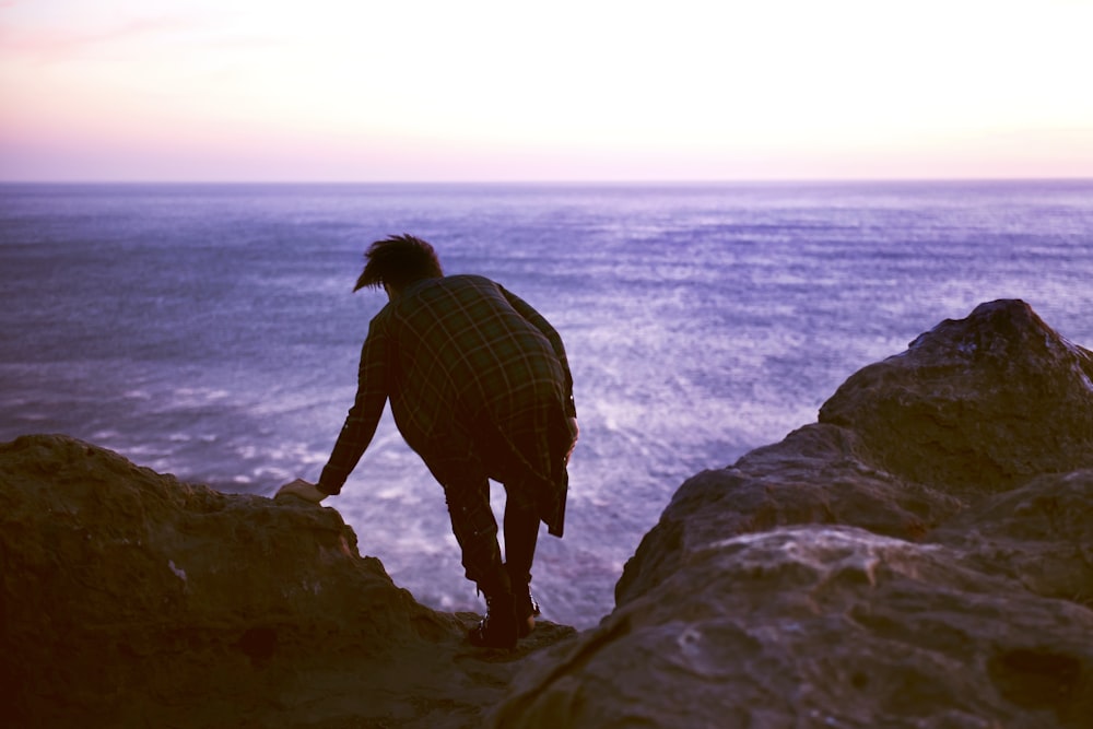 man on top of rock beside body of water