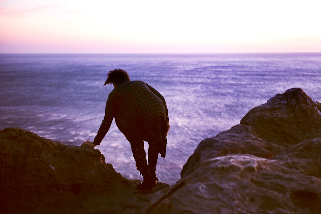 man on top of rock beside body of water