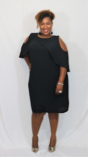 A smiling customer wearing a simple, elegant dress from ChicEthic, standing against a soft pastel wall.