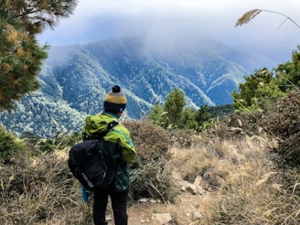 A model wearing a hemp jacket and trousers standing on a trail with the Himalayas fading into mist behind.