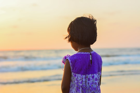 girl in white and purple dress standing on seashore facing the golden hour in Kozhikode Beach India