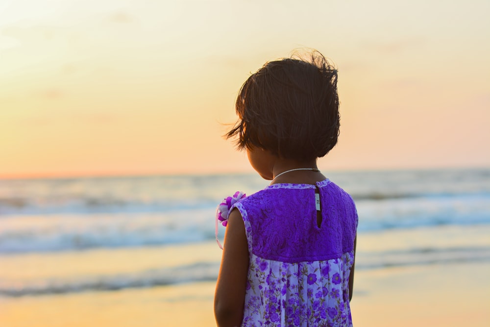 girl in white and purple dress standing on seashore facing the golden hour