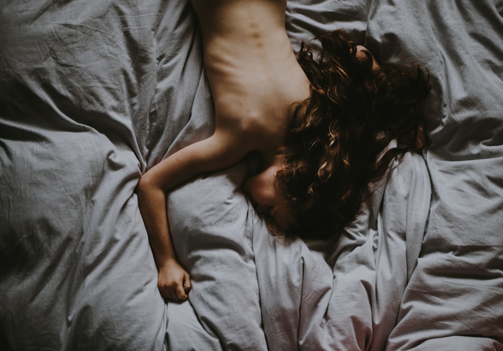 灰色のベッドカバーに横たわっている裸の女性
