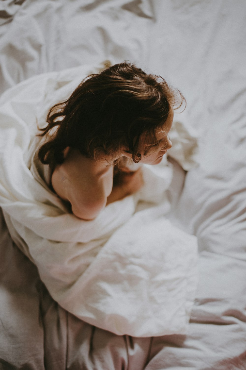 Frau sitzt auf Bett, bedeckt mit weißer Decke