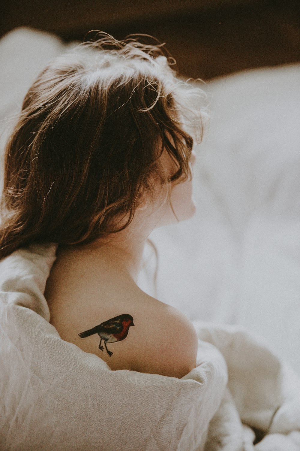 mujer con tatuaje de pájaro en el hombro sobre una superficie blanca