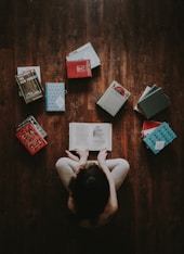 flat lay photography of woman sitting on brown wooden parquet flooring surrounded by books