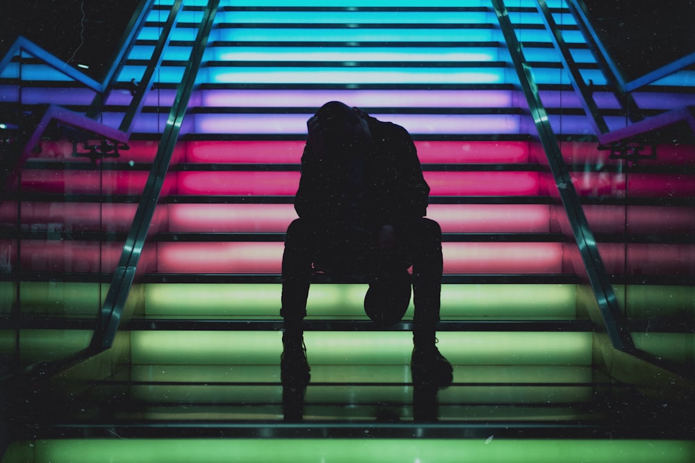 silhouette photo of man sittin on multicolored stair