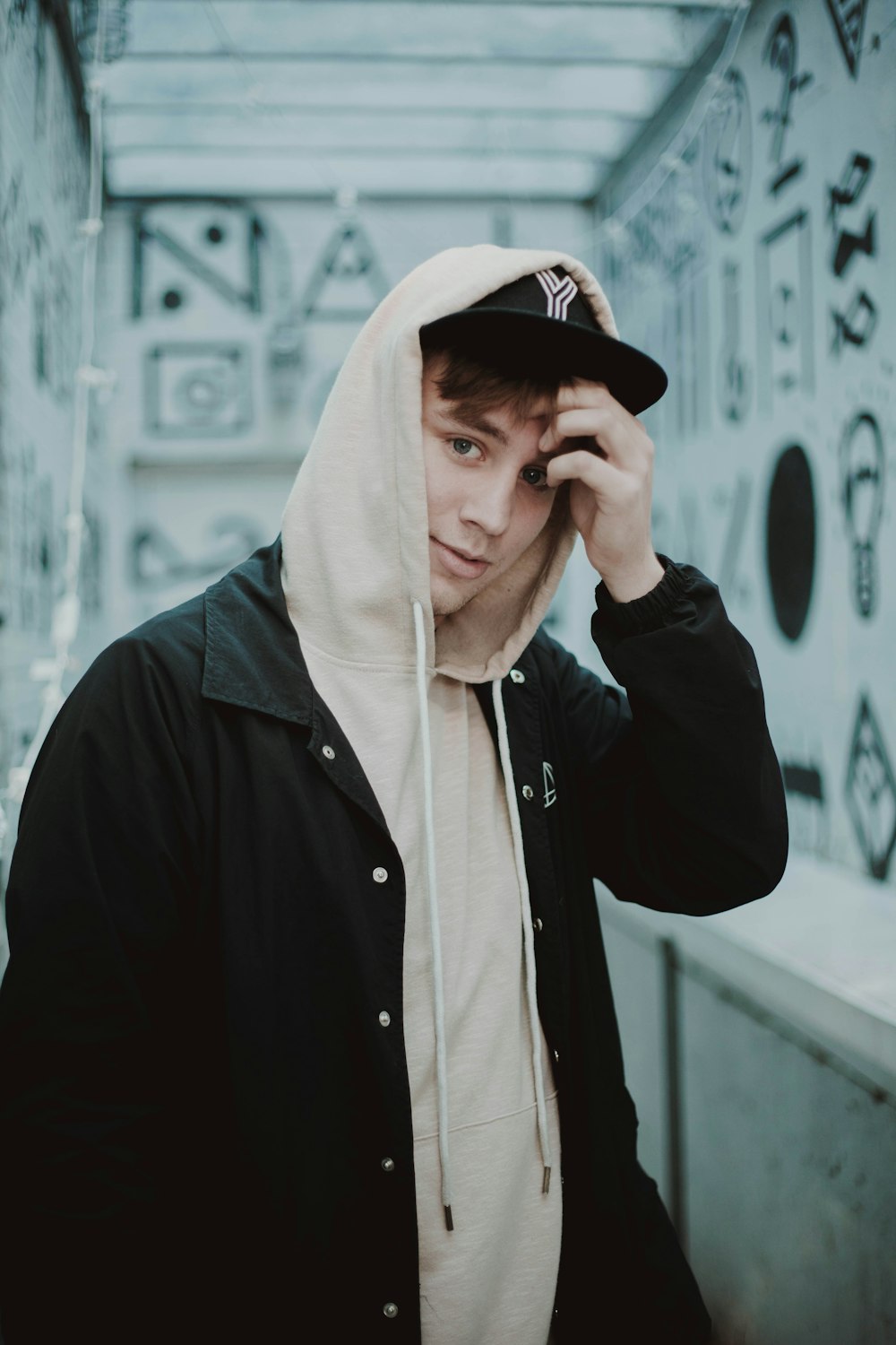 man in hoodie standing near white painted wall