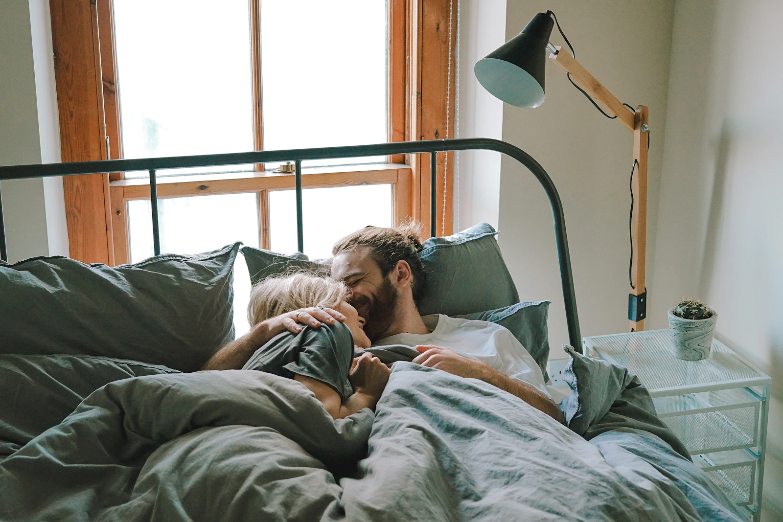A couple lying together in bed laughing, warm window light
