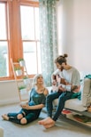 man sitting on sofa playing guitar looking at girl sitting on the ground near window inside room