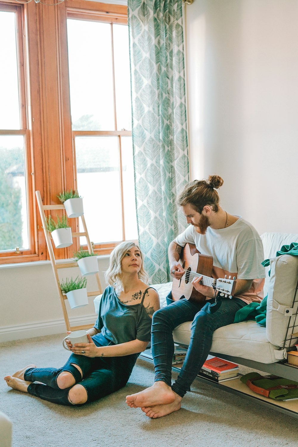 homme assis sur le canapé jouant de la guitare regardant fille assise sur le sol près de la fenêtre à l’intérieur de la chambre