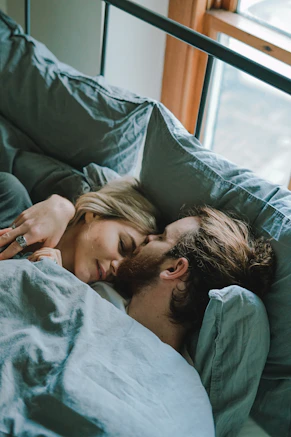 man kissing woman's forehead while lying on bed