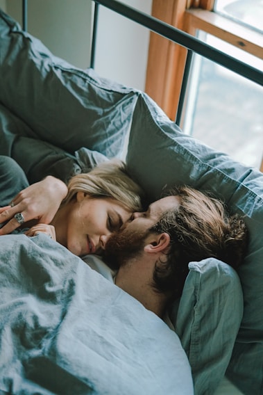 A cozy bedroom scene featuring a man and woman wearing huggedby sleepwear, smiling and relaxed.