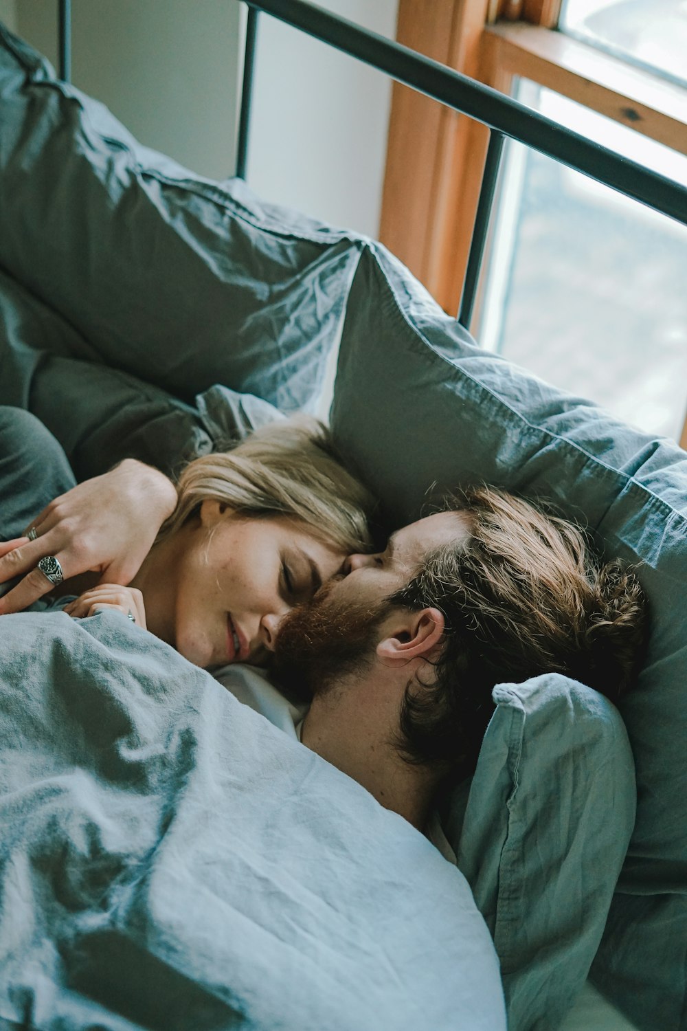 homem beijando a testa da mulher enquanto deitado na cama