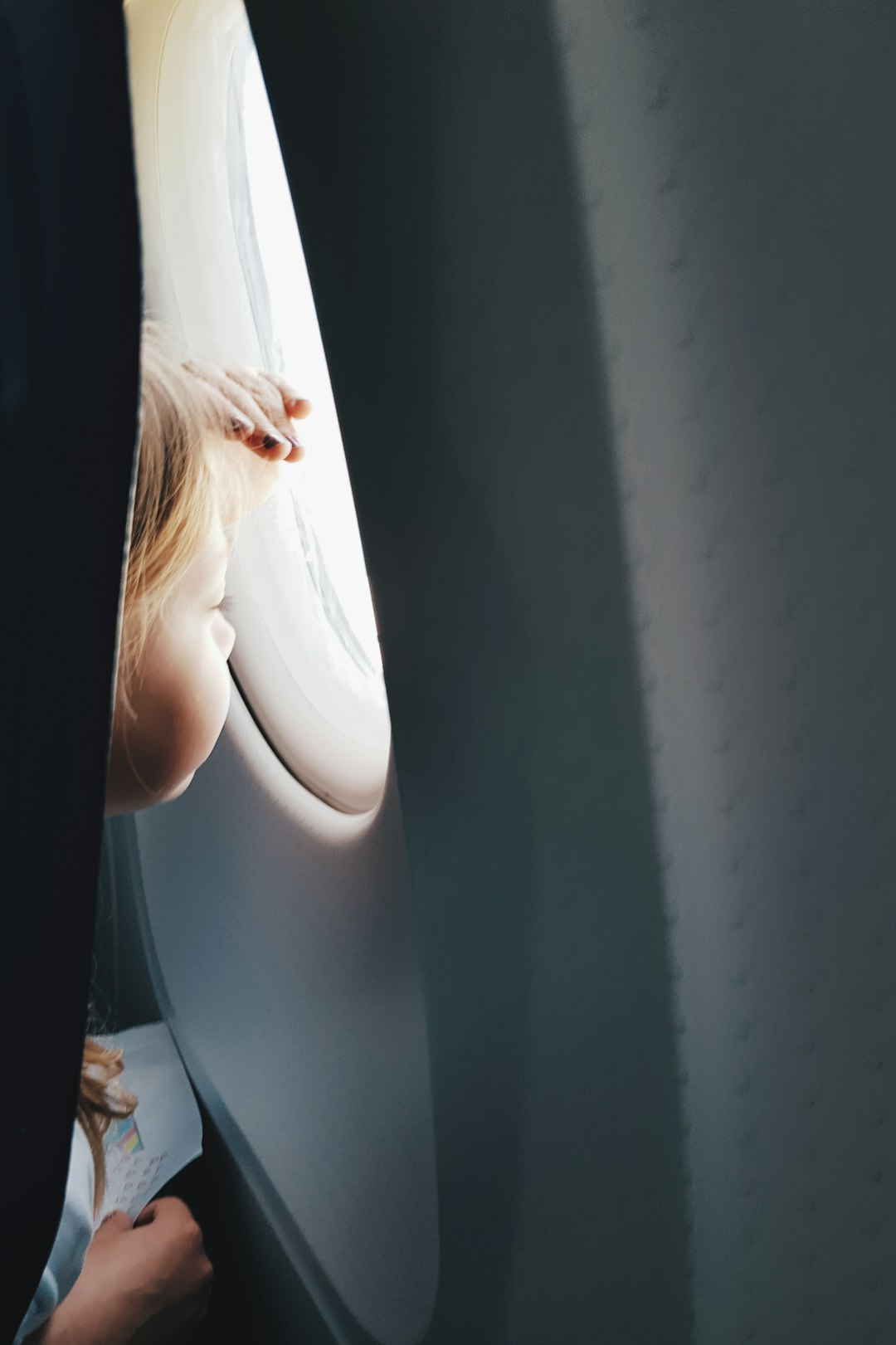 A young child looking out of an airplane window mid-flight