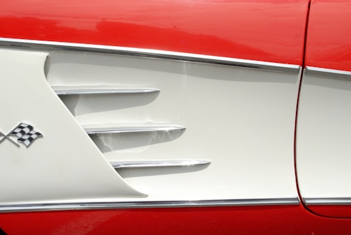 The image features a close-up view of a vintage car exterior with a red and white color scheme. The design includes chrome accents and a checkered flag emblem, suggesting a classic or retro appeal.