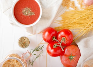 four red tomatoes beside pasta and bowl