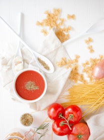 four red tomatoes beside pasta and bowl