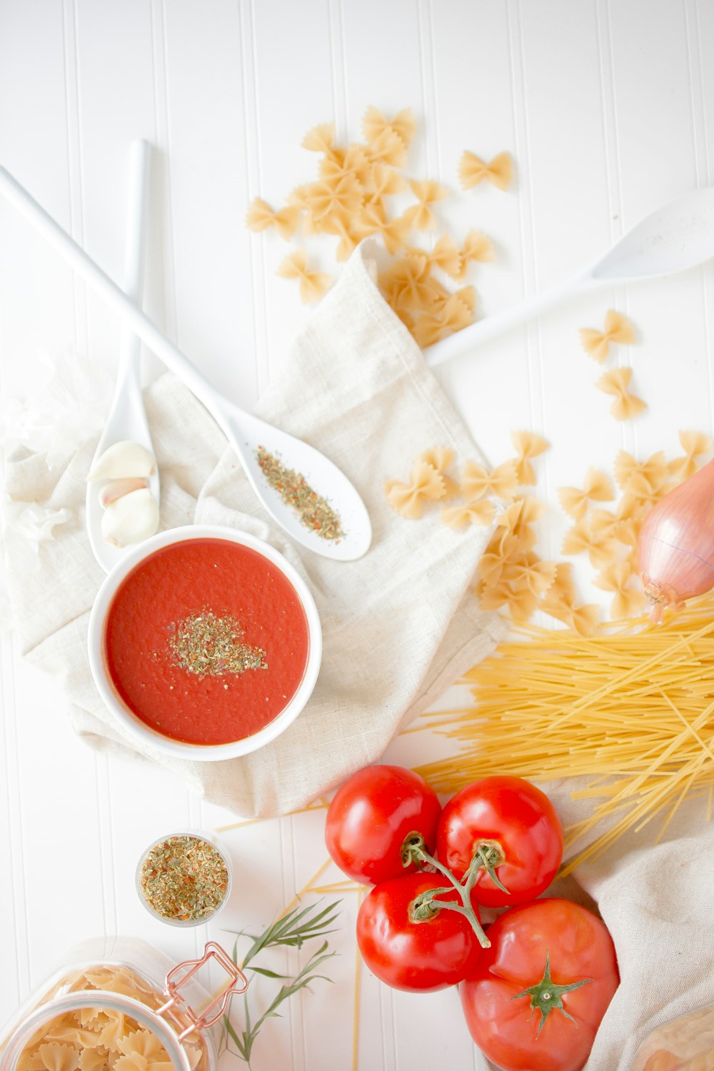 Quattro pomodori rossi accanto alla pasta e alla ciotola