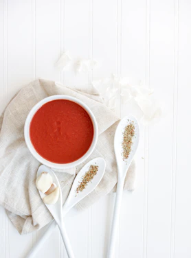 A soft pastel green-themed flat lay of a baby’s first meal with fresh veggies and a colorful spoon on a clean white background.