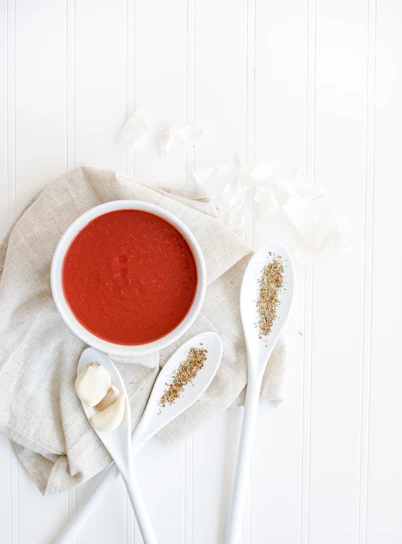 A soft pastel green-themed flat lay of a baby’s first meal with fresh veggies and a colorful spoon on a clean white background.