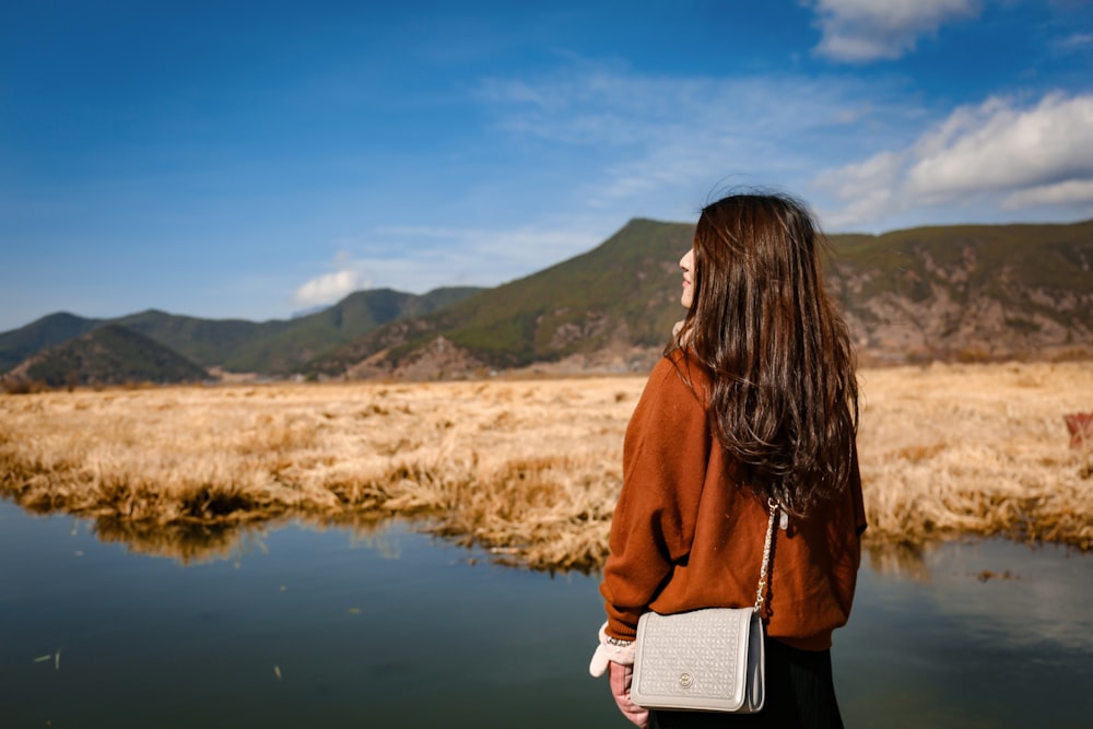 Mujer de pie frente a la montaña verde bajo el cielo azul