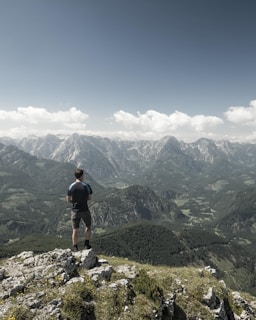 man standing on cliff while staring at the mountain