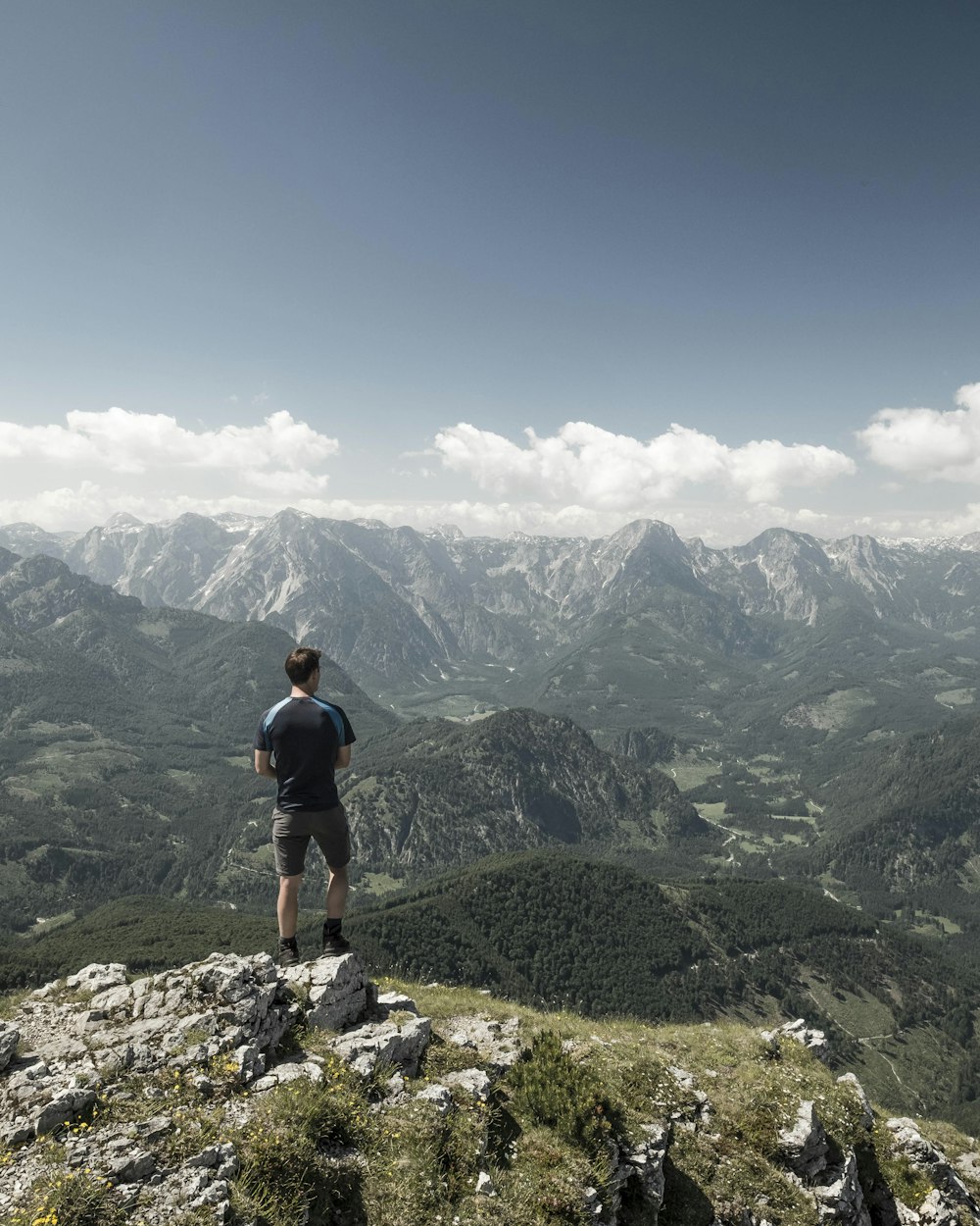 man standing on cliff while staring at the mountain