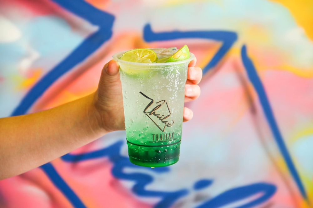 person holding clear plastic cup filled with clear liquid and sliced lime