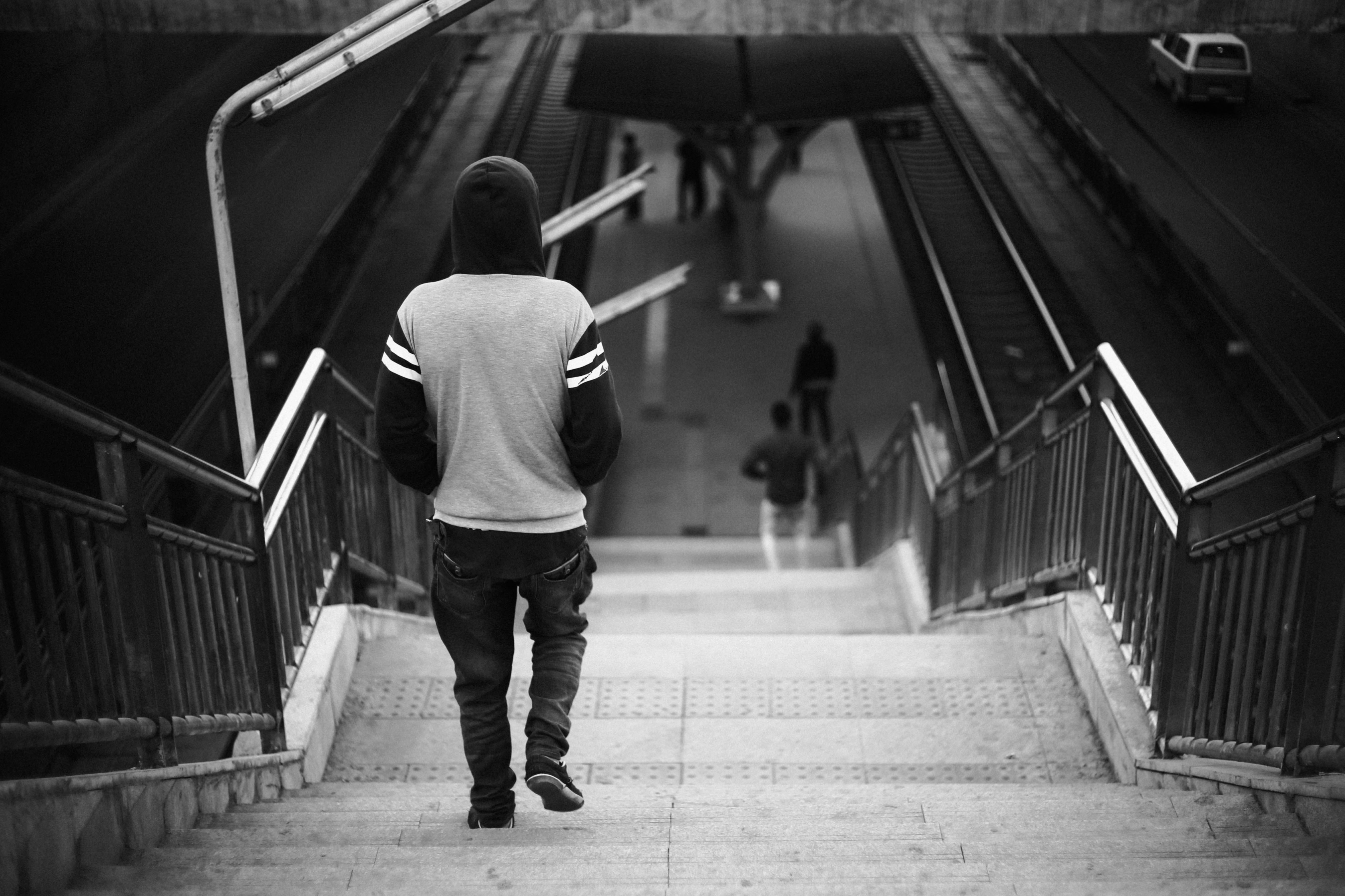 grayscale photo of person wearing hoodie walking on stairs