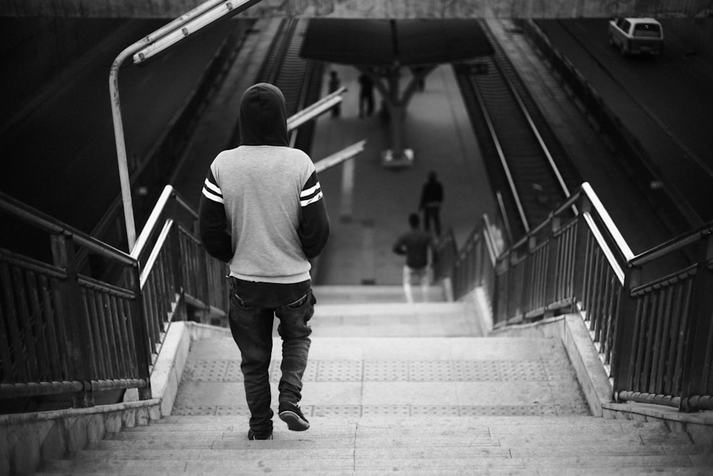 grayscale photo of person wearing hoodie walking on stairs
