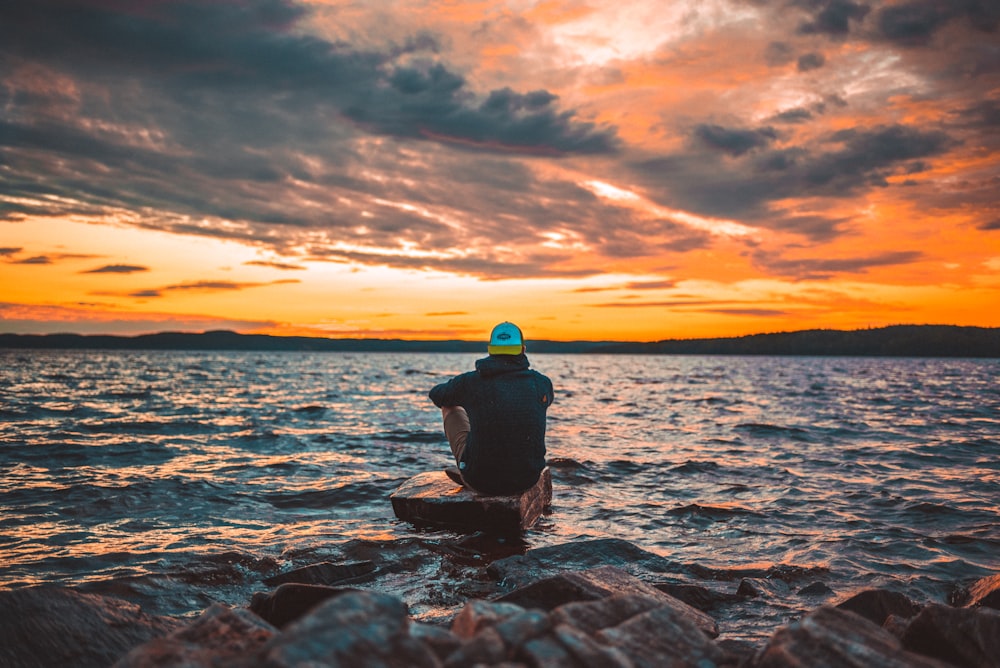 man sitting on gray rock during sunset